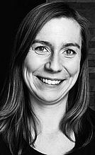 Ein Porträt einer lächelnden Frau mit langen, glatten Haaren. Sie trägt ein schwarzes Oberteil und hat einen freundlichen Ausdruck. Der Hintergrund zeigt eine strukturierte Wand.