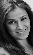 Ein lächelnder Mensch mit langen, glatten Haaren, der in die Kamera schaut. Die Aufnahme ist in Schwarz-Weiß gehalten, wodurch die Gesichtszüge und der Ausdruck der Person hervorgehoben werden.